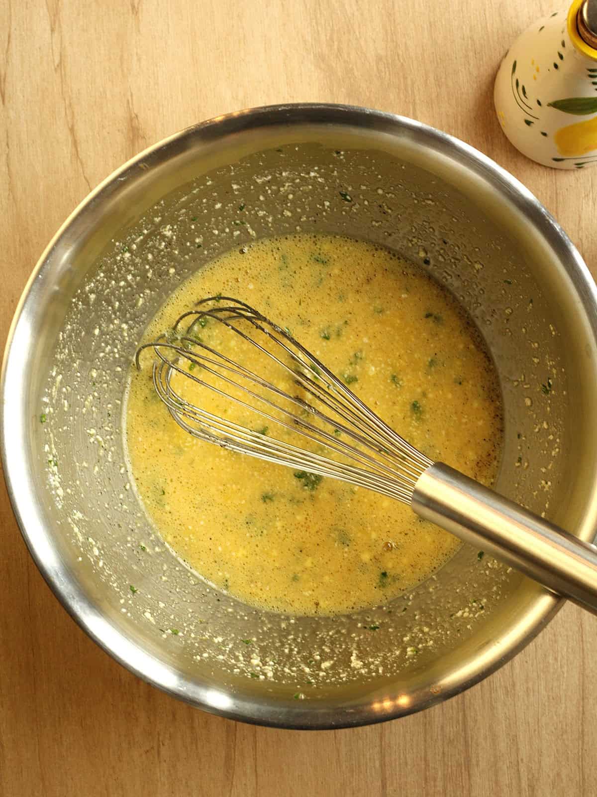 Whisked eggs, parsley and Parmigiano cheese in bowl for baked frittata recipe.