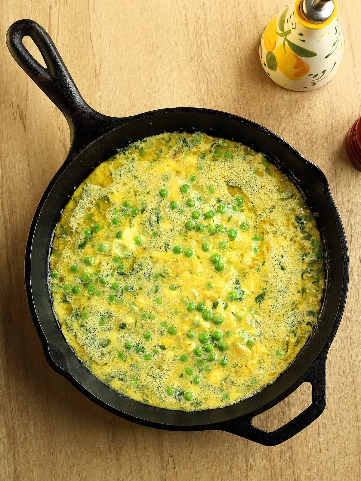 Cast iron skillet with frittata with peas mixture ready for the oven.