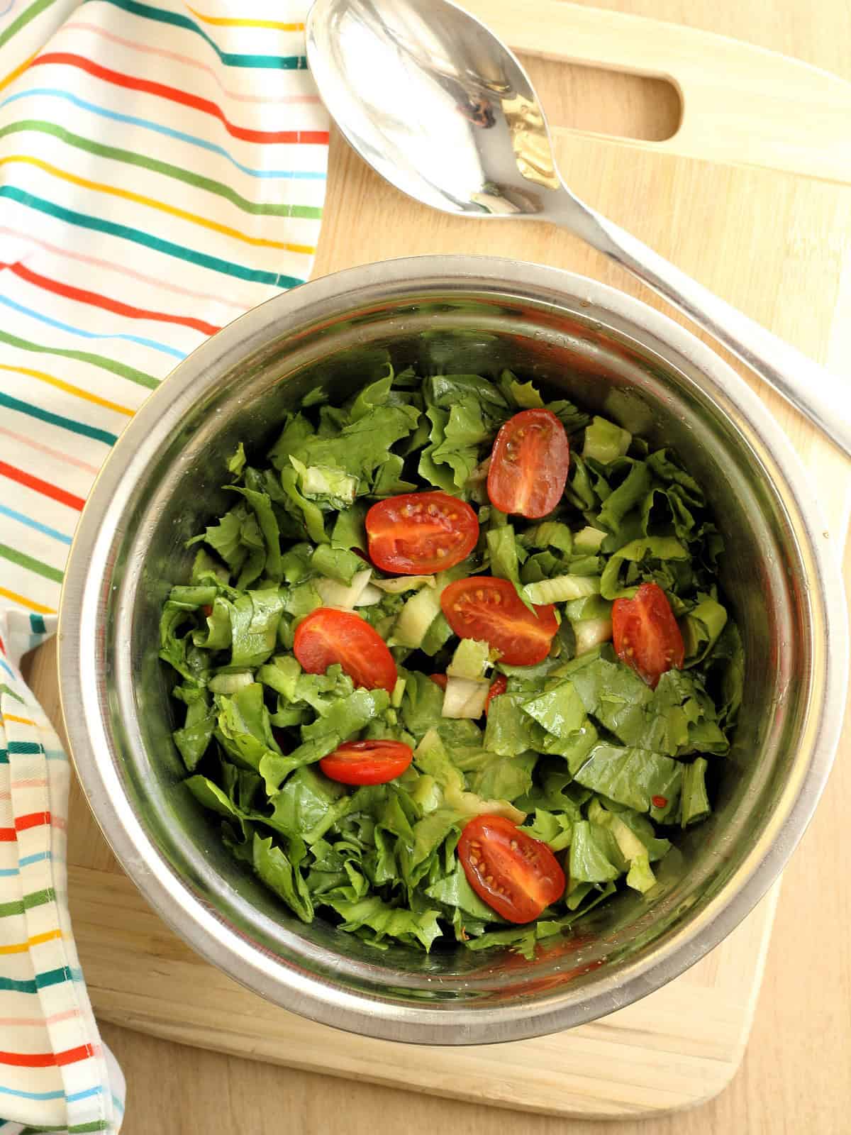 Chopped escarole and halved cherry tomatoes tossed with salt and olive oil in bowl.