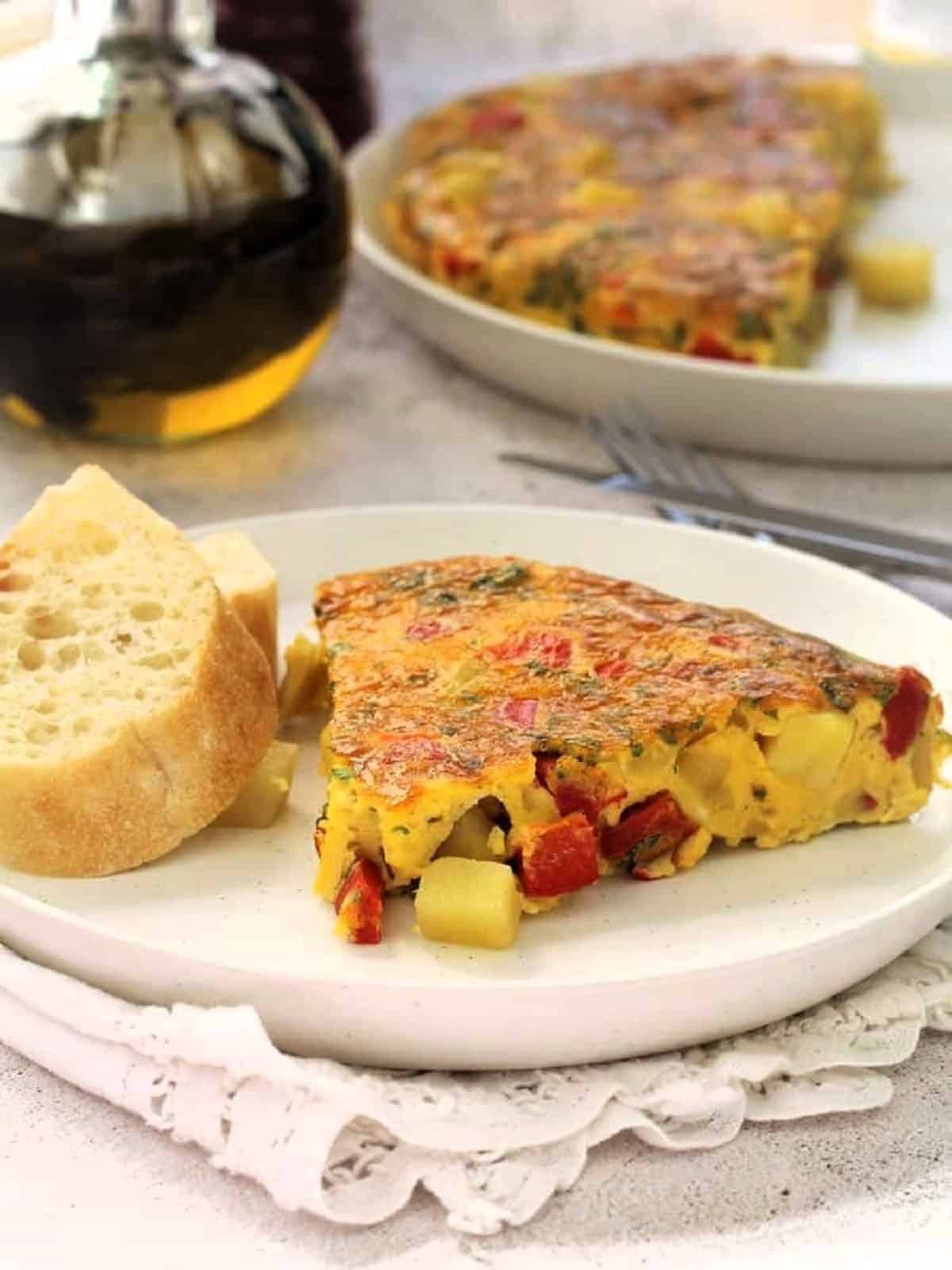 Wedge of baked potato and red pepper frittata on plate with sliced bread.