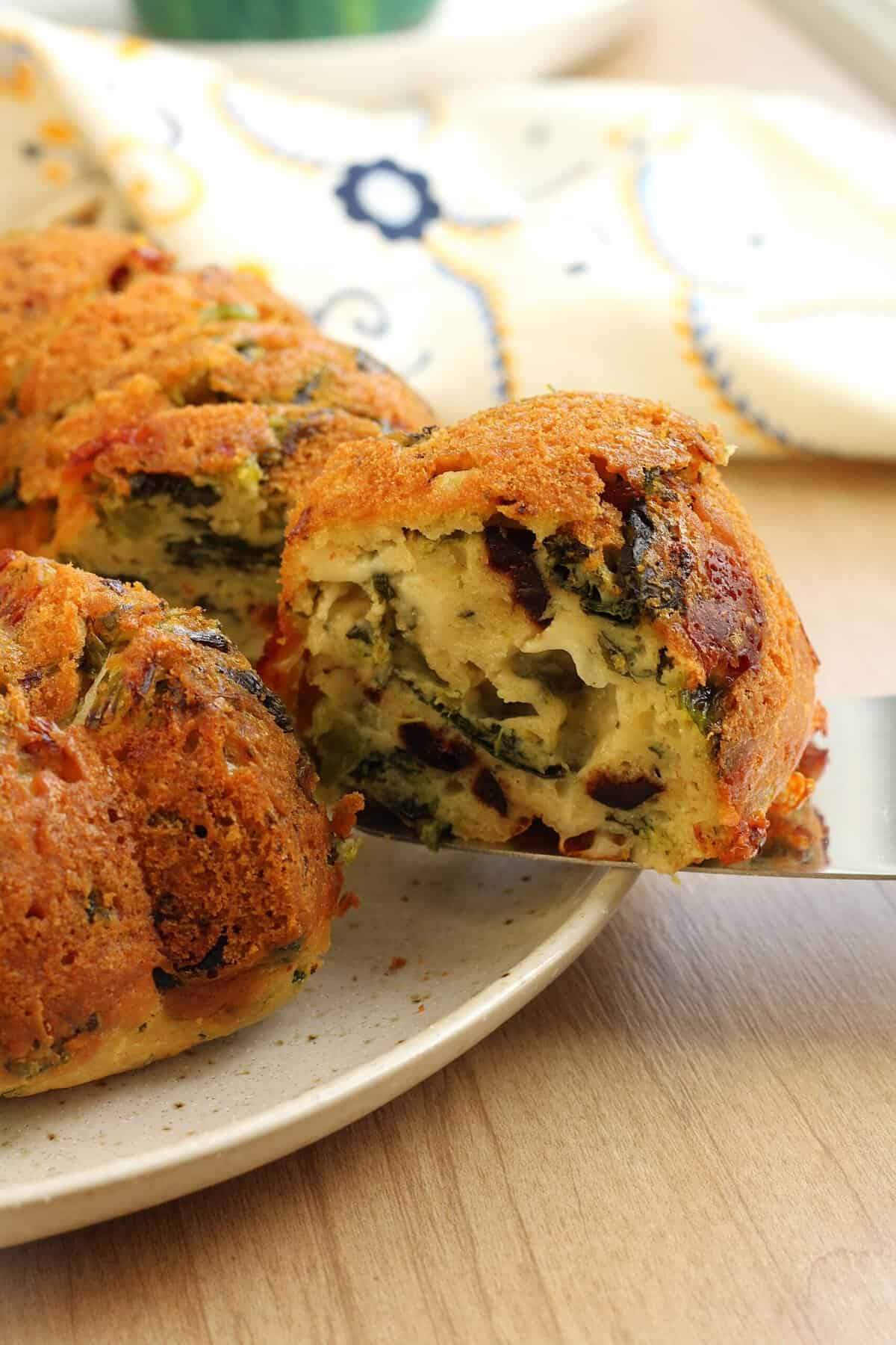 Slice of savory ring cake (ciambella salata) with rapini and cheese served from whole cake.