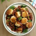 Sicilian swordfish meatballs in sweet and sour sauce topped with fresh mint leaves in bowl.