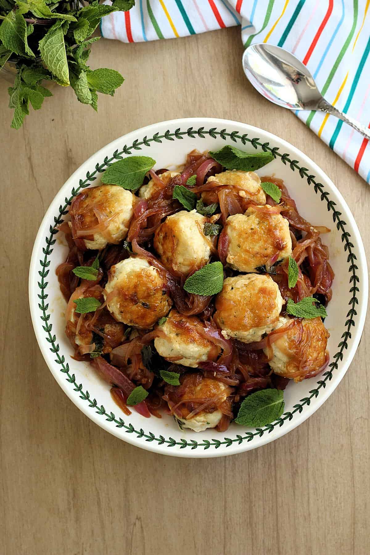 Sicilian swordfish meatballs in sweet and sour sauce topped with fresh mint leaves in bowl.