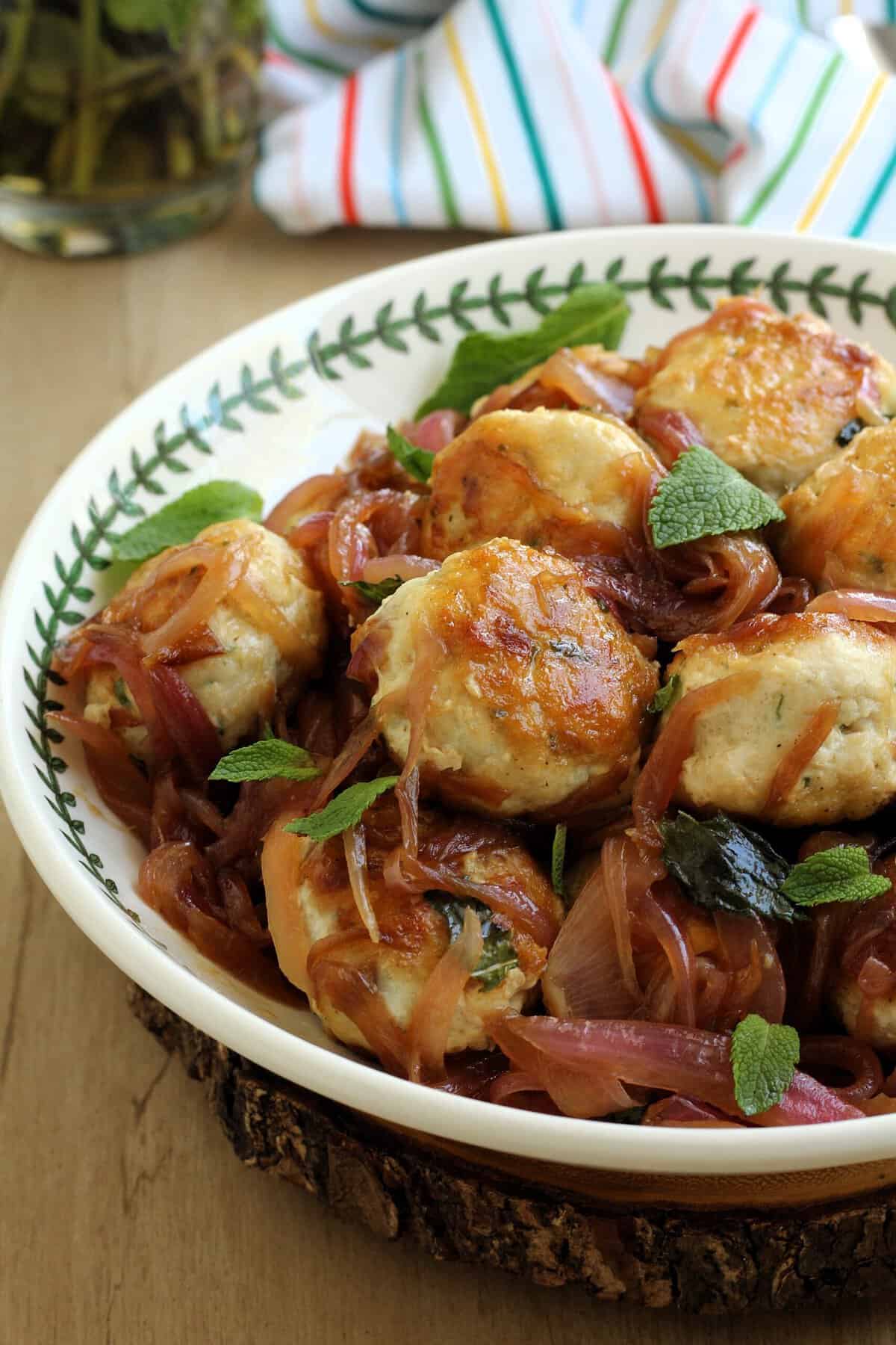 Swordfish meatballs in Sicilian sweet and sour sauce with red onion in bowl topped with fresh mint.