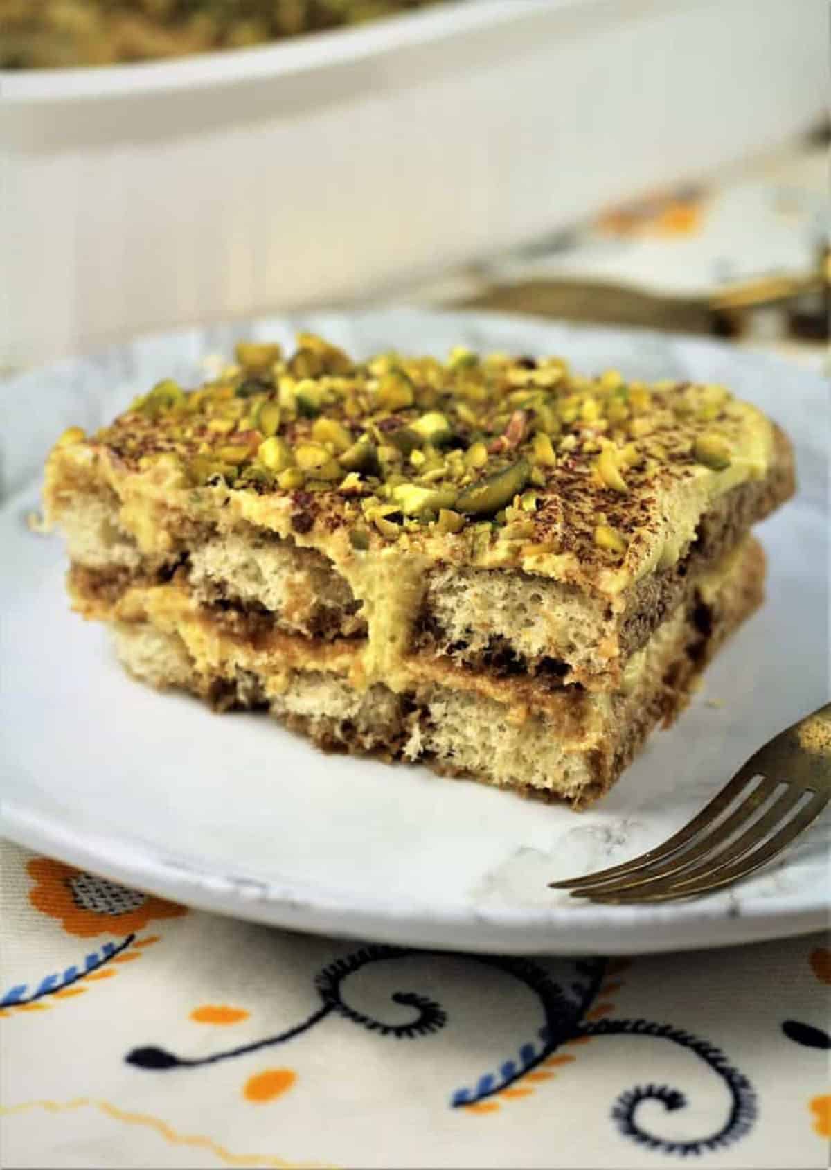 Square of tiramisu with pistachios on plate with fork.