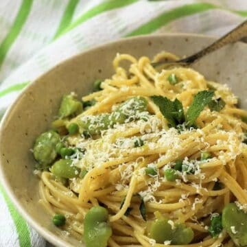 Bowl of pasta with fava beans and peas topped with grated cheese.