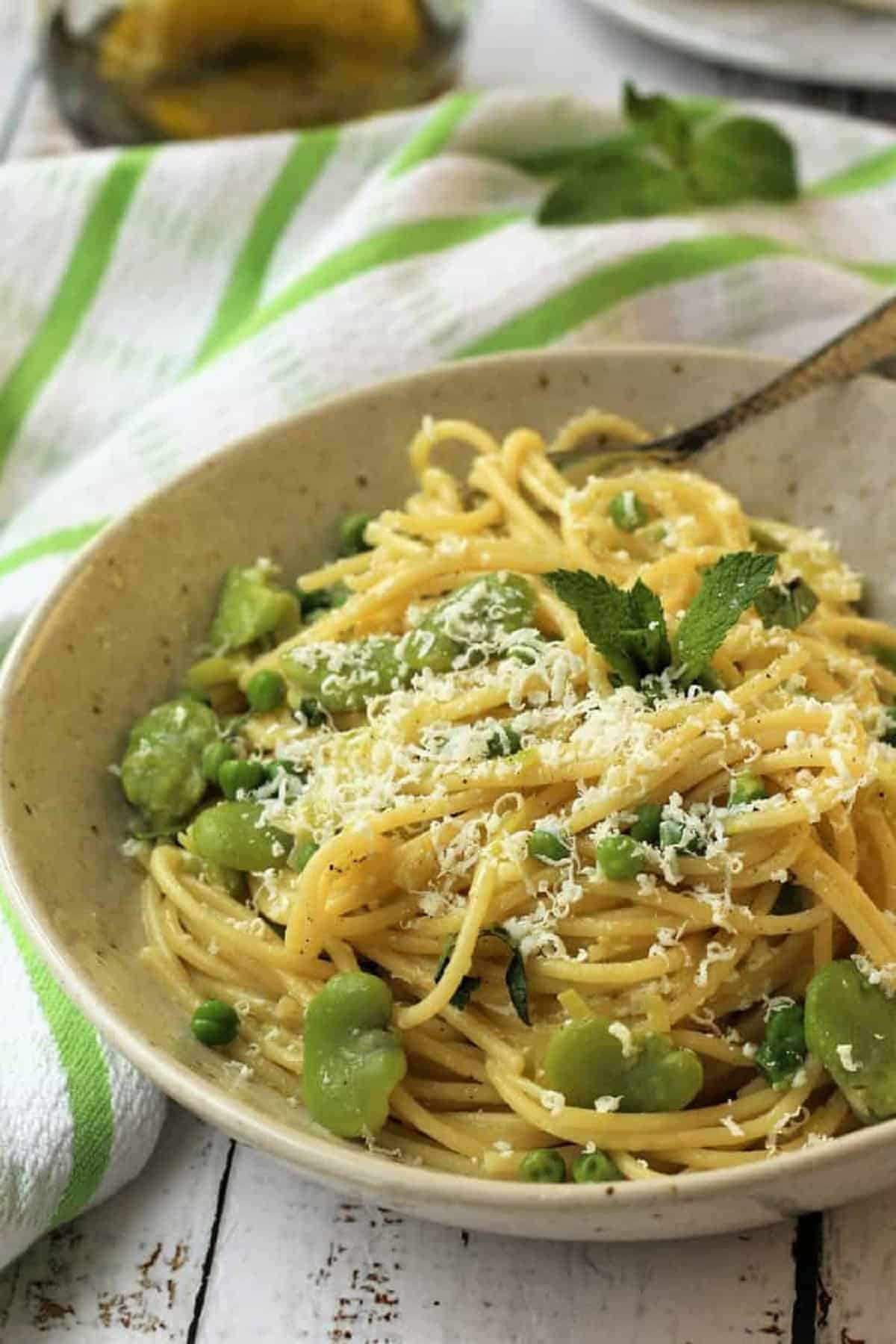 Bowl of pasta with fava beans and peas topped with grated cheese.