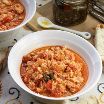 Italian fried eggs with tomatoes in bowl surrounded by bread slices.