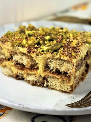 Tiramisu with pistachio cream and chopped pistachios on top on plate with fork.