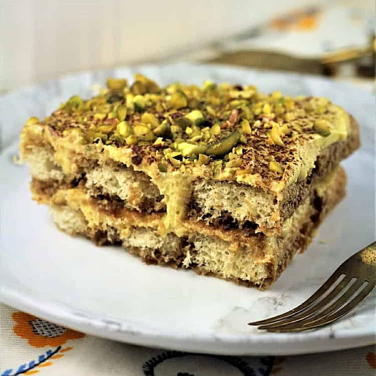Tiramisu with pistachio cream and chopped pistachios on top on plate with fork.