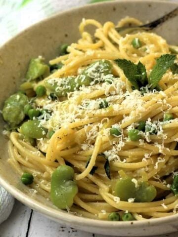 Bowl of pasta with fava beans and peas topped with grated ricotta salata.