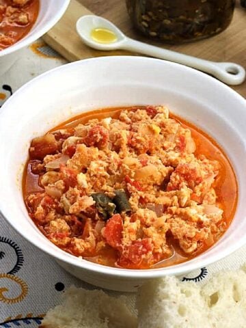 Fried eggs with tomatoes in bowl with slices of bread next to it.