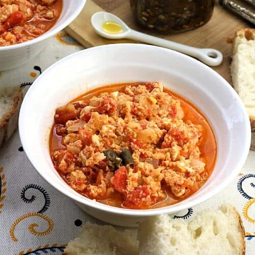 Fried eggs with tomatoes in bowl with slices of bread next to it.