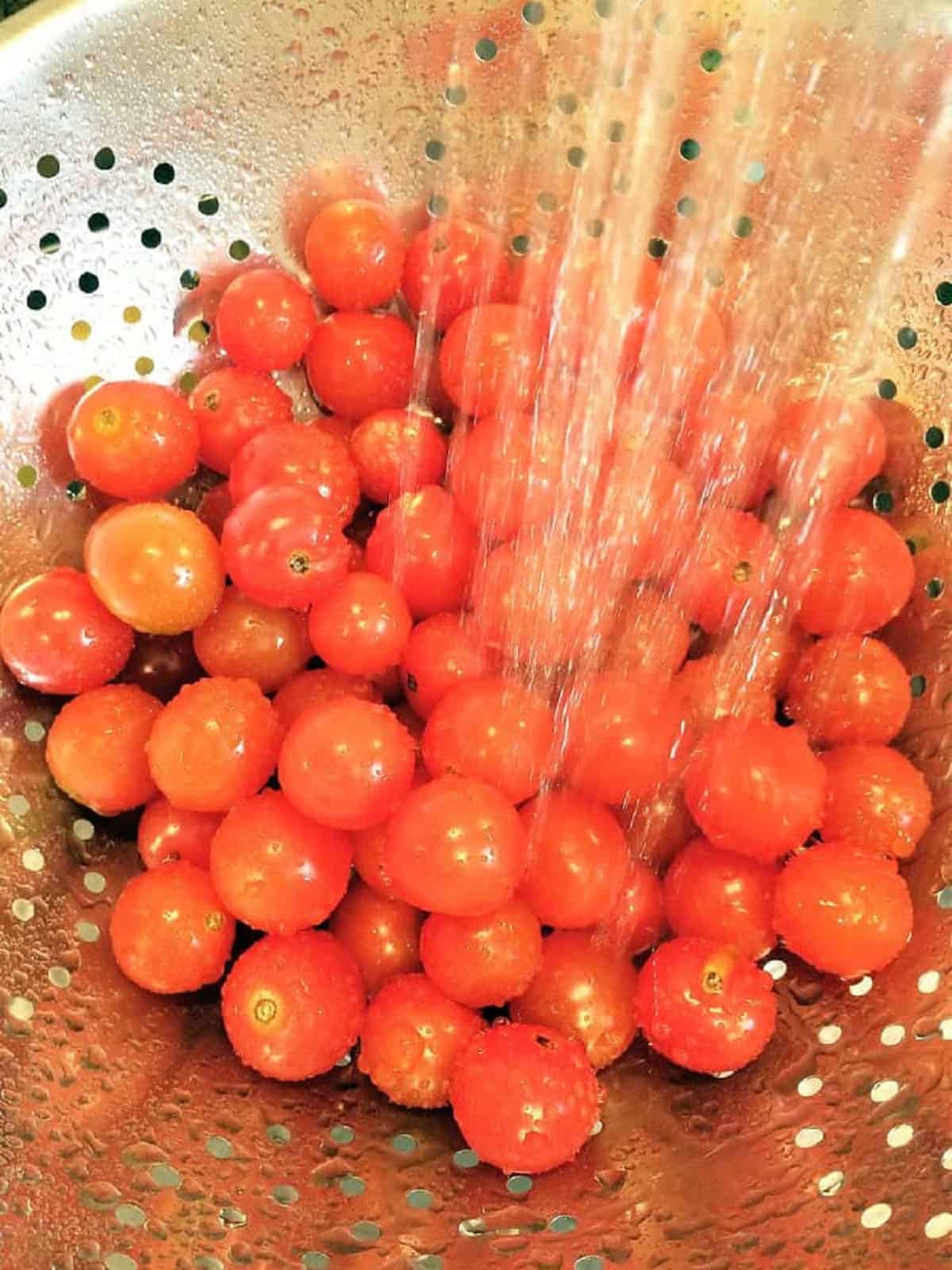 Cherry tomatoes washed in a colander under running water. 