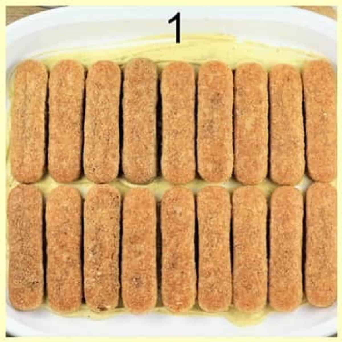 Savoiardi cookies layered over pistachio cream in casserole dish for tiramisu recipe.
