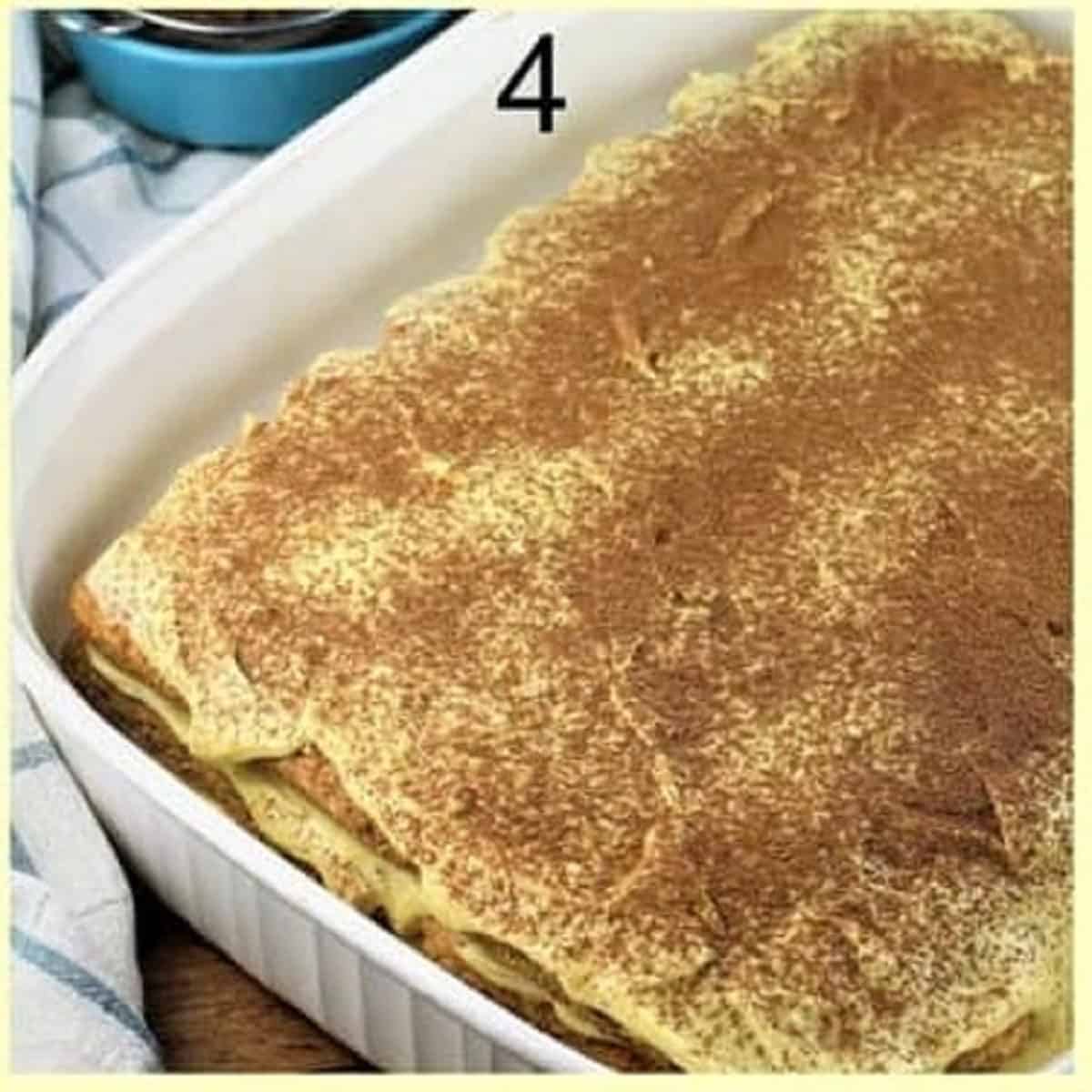 Cocoa powder dusted over pistachio tiramisu in casserole dish.