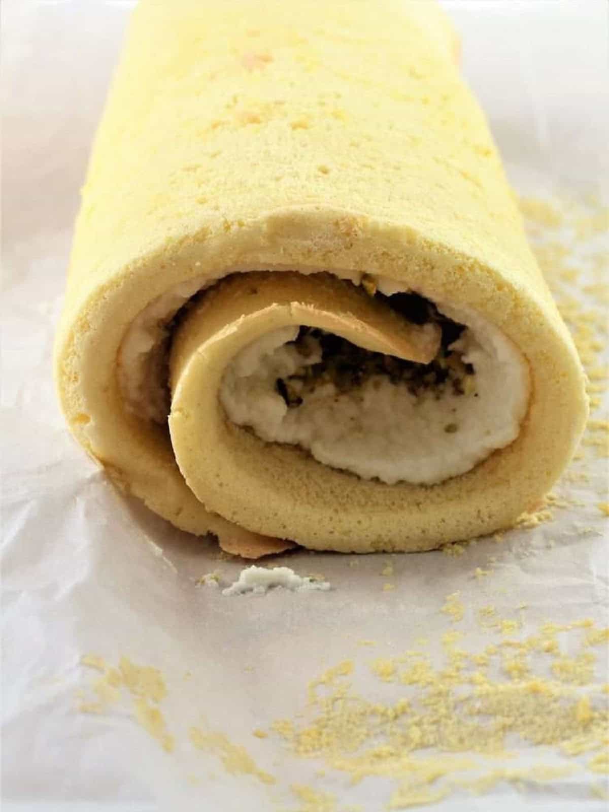 Sponge cake roll filled with ricotta cream and pistachios on parchment paper.