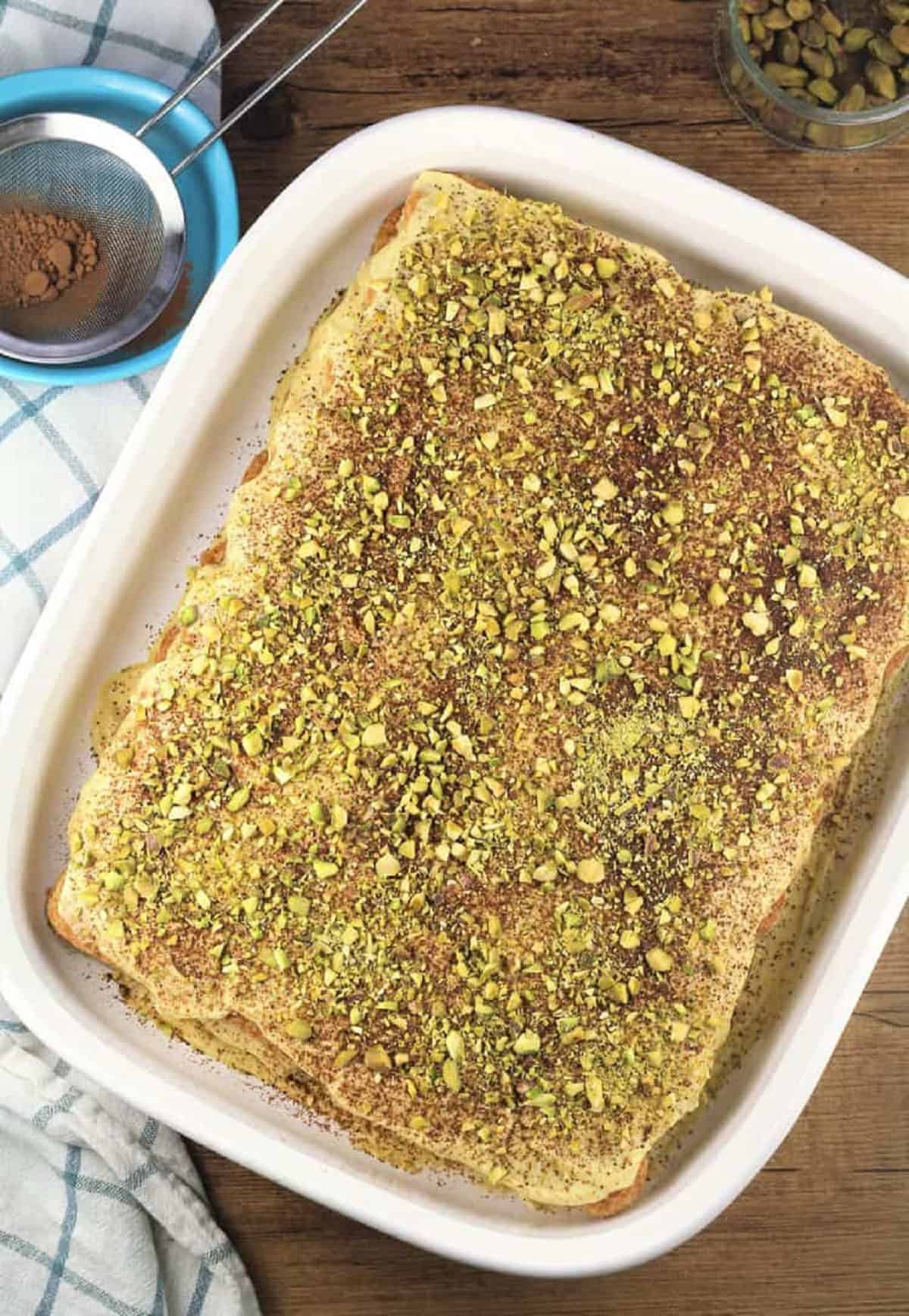 Pistachio tiramisu covered with chopped pistachios in white caserole dish.