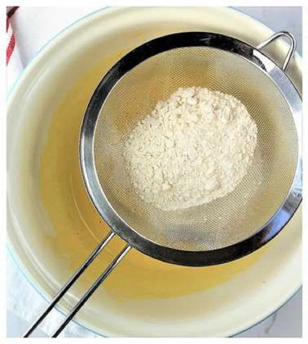 Whisked flour over bowl with wet ingredients for roll cake recipe.