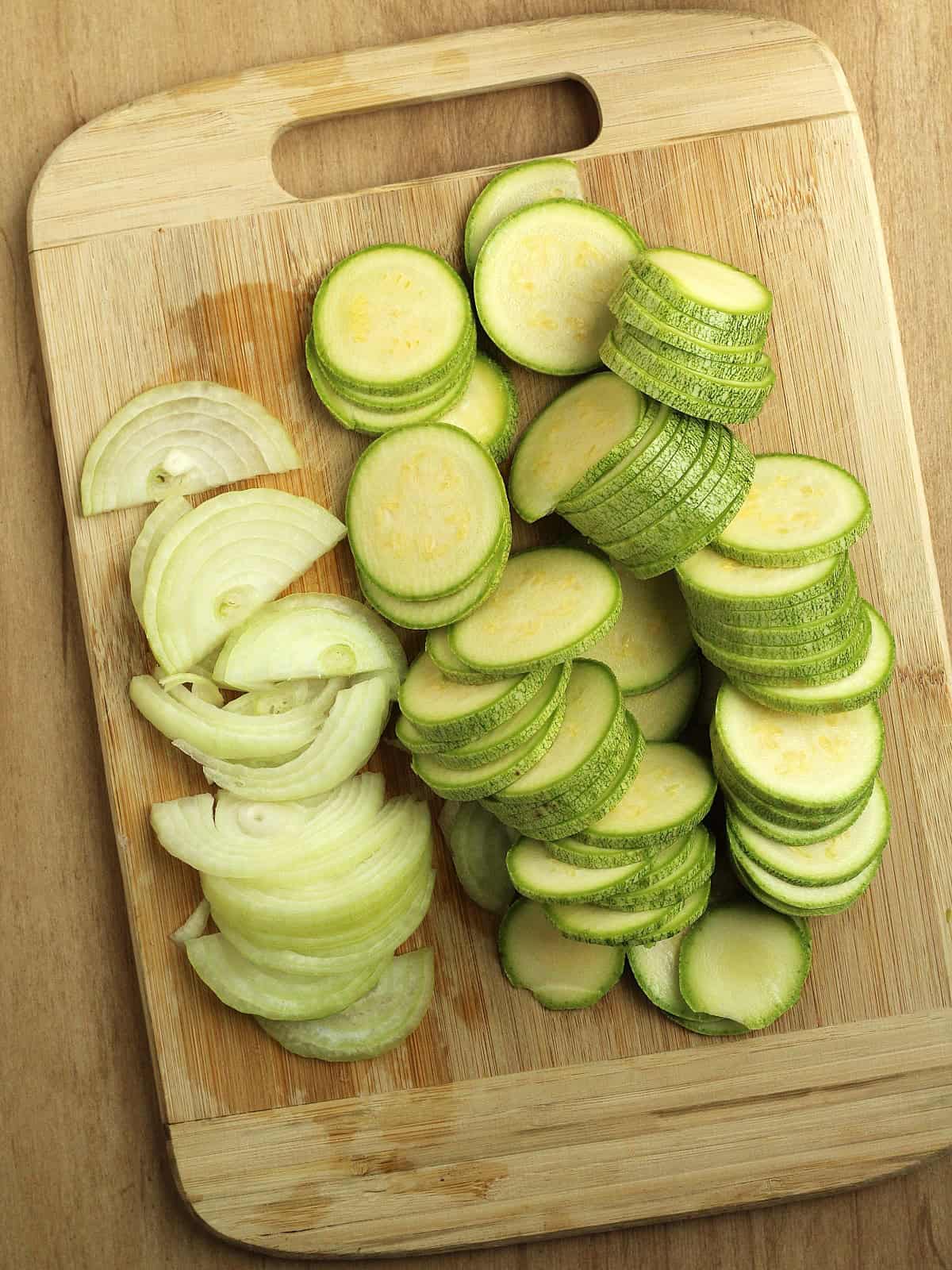 Thinly sliced zucchini rounds and onion on wood board for flatbread recipe.