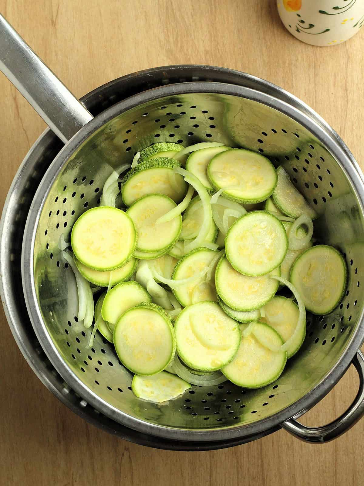 Zucchini and onion slices coated with salt in colander over bowl.