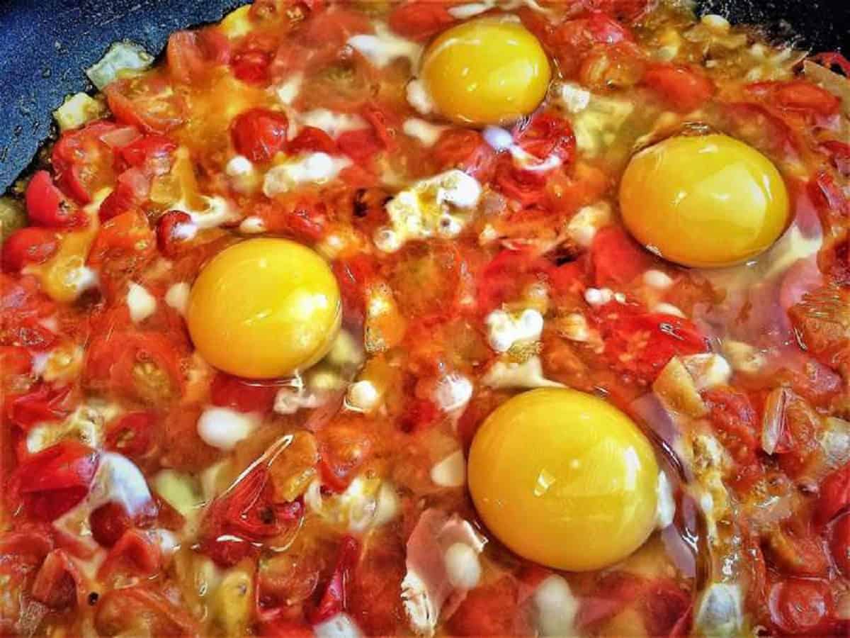Eggs added to skillet with tomatoes and diced onions.