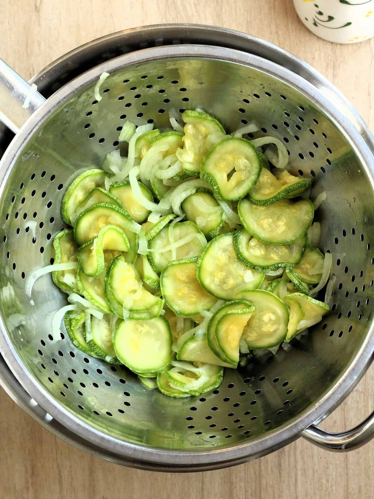 Salted zucchini and onion slices in colander to draw out excess water.