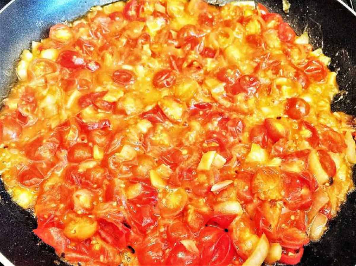 Fried tomatoes with eggs scrambled in them in skillet.