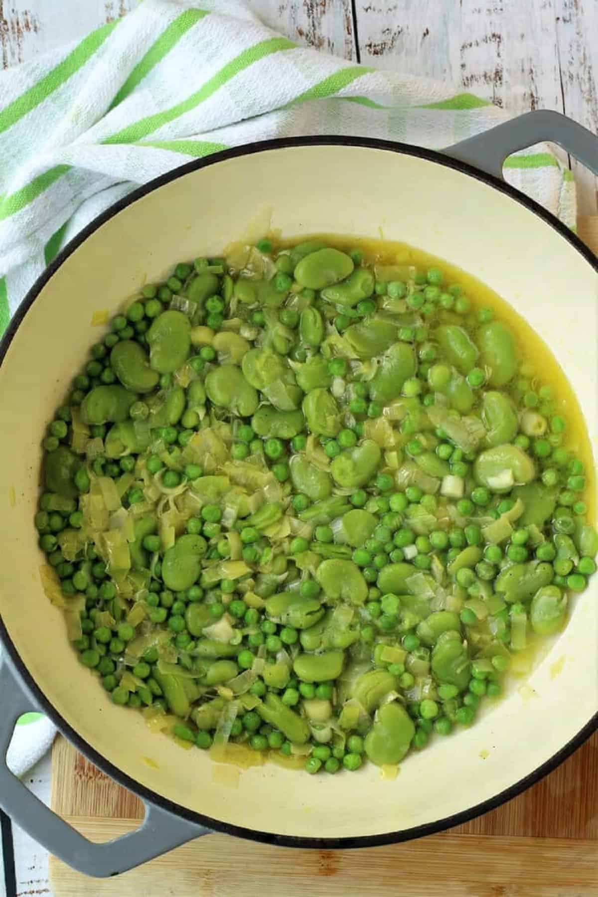 Fava beans, peas and leek simmering in skillet.