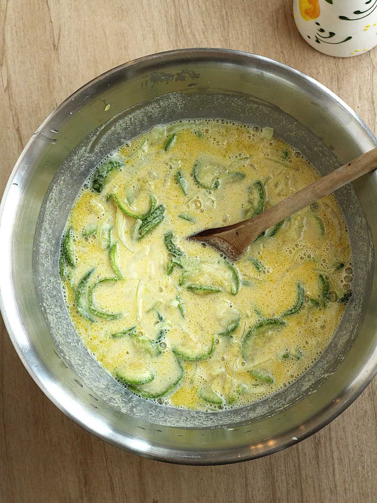Zucchini and onion slices stirred into bowl with chickpea flour mixture.