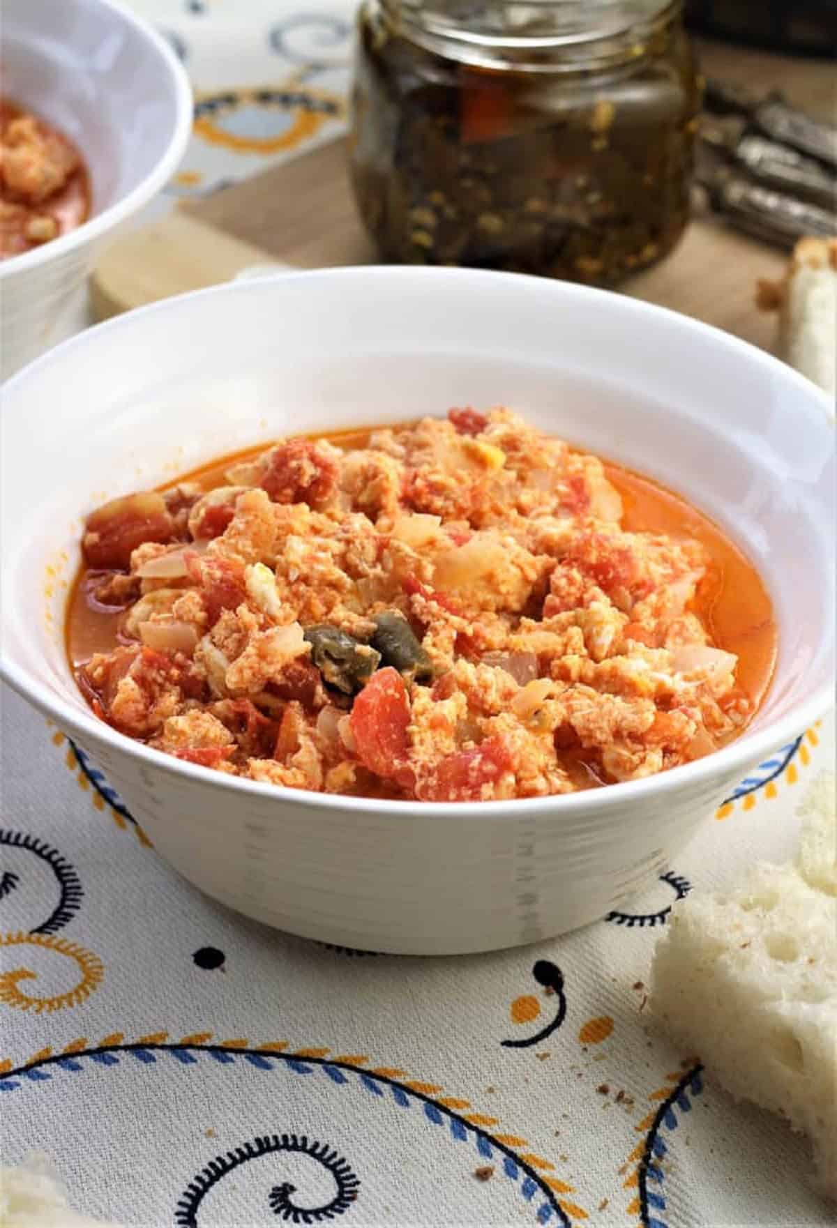 Italian fried tomatoes with eggs in bowl with sliced bread.