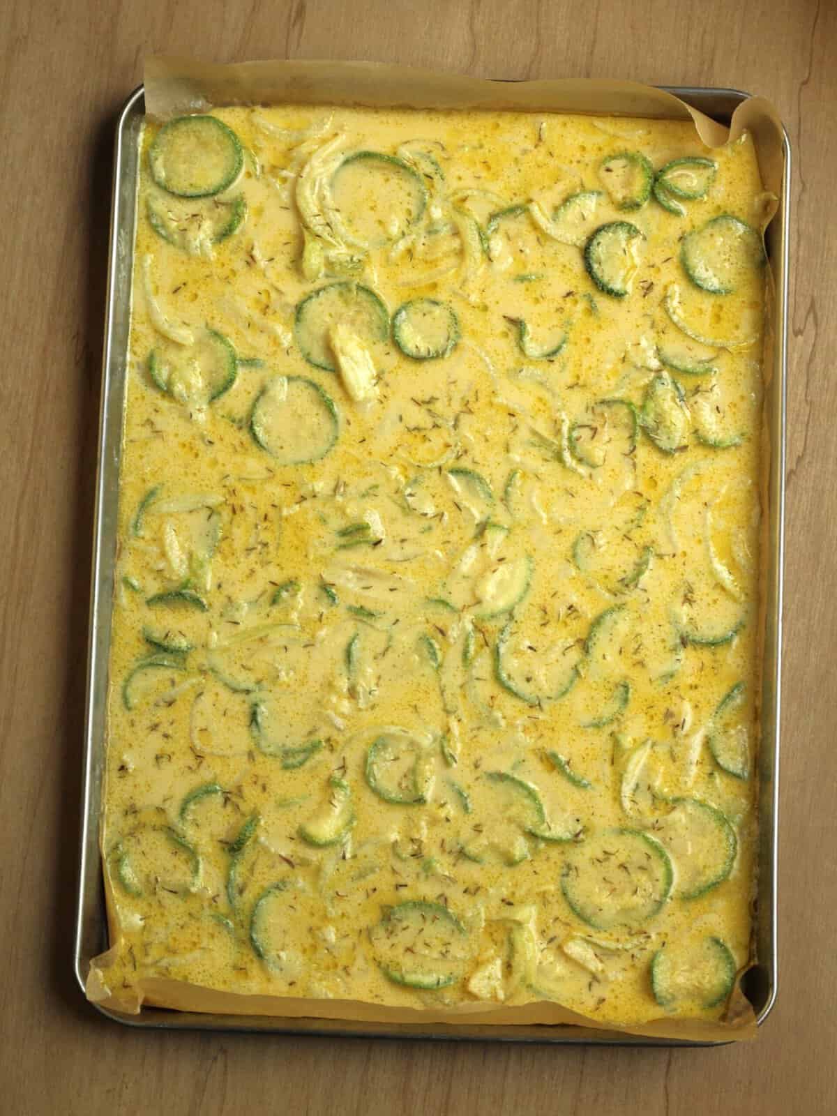 Chickpea farinata batter with zucchini and onions poured into sheet pan.