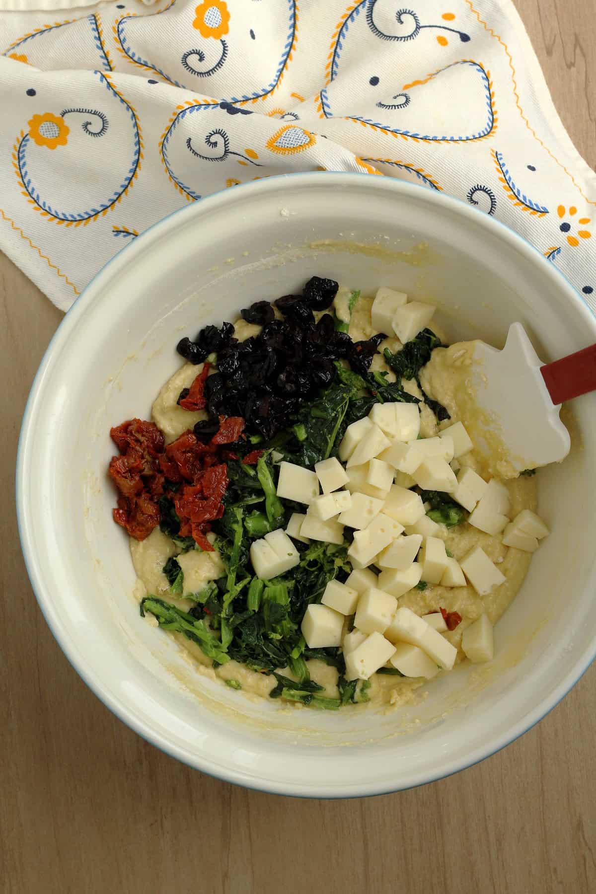 Cheese, olives, sun dried tomatoes and rapini added to bowl with batter for savory cake.