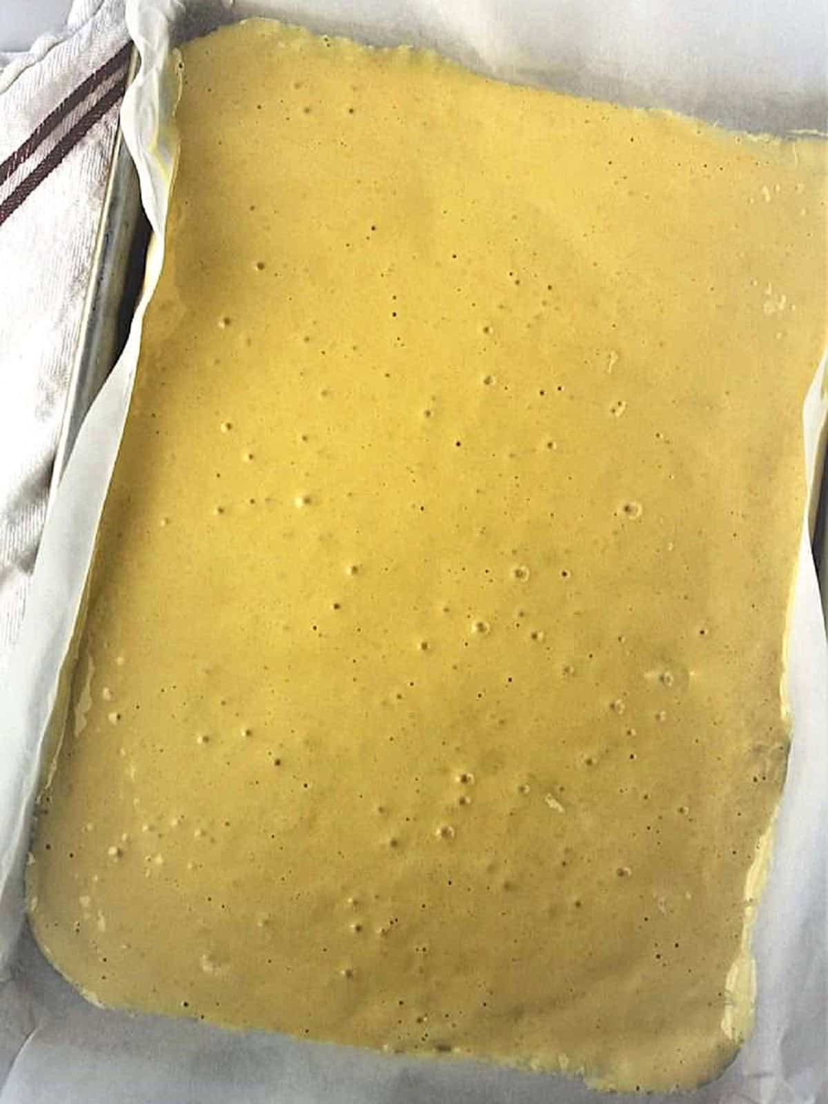 Cake roll batter poured into sheet pan covered with parchment paper.