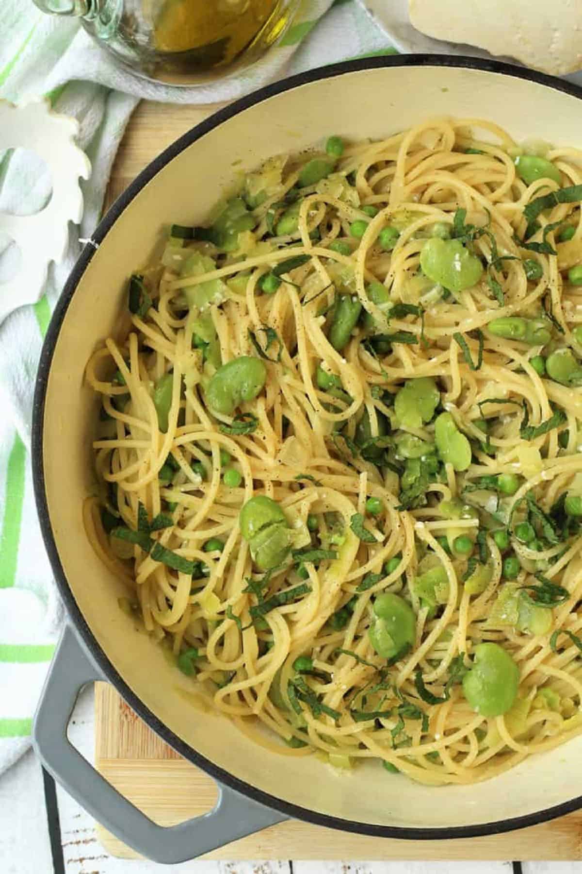 Skillet filled with spaghetti with fava beans and peas topped with fresh mint.