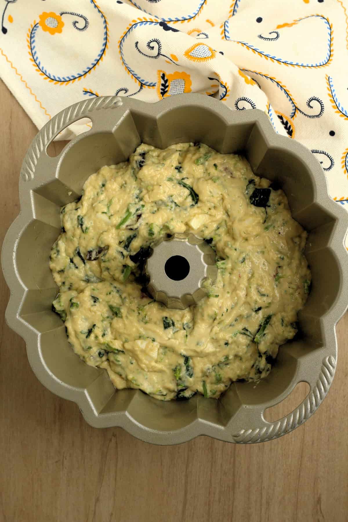 Savory ring cake batter with rapini poured into prepared bundt pan.