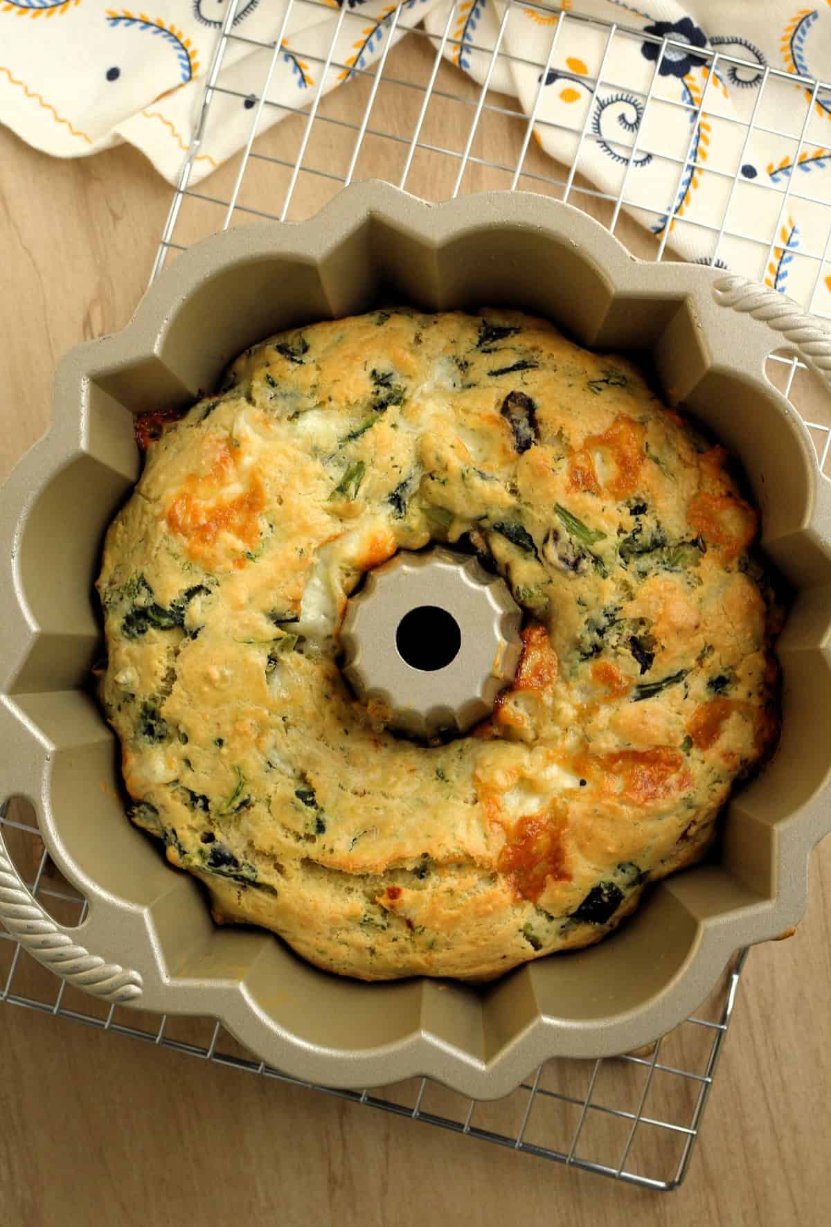 Savory ring cake baked in bundt pan resting on wire rack.