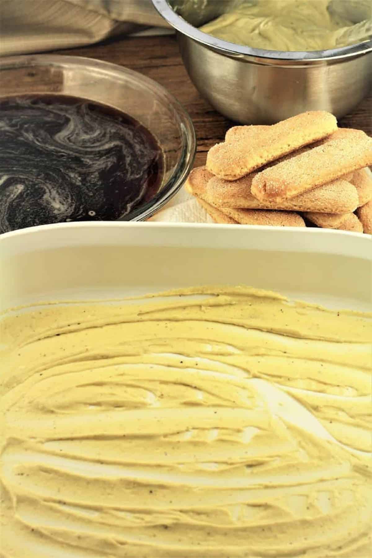 PIstachio mascarpone cream smeared on bottom of casserole dish for tiramisu recipe.