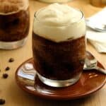 Glasses filled with coffee granita topped with whipped cream on dish with spoon.