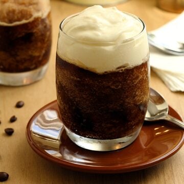 Glasses filled with coffee granita topped with whipped cream on dish with spoon.