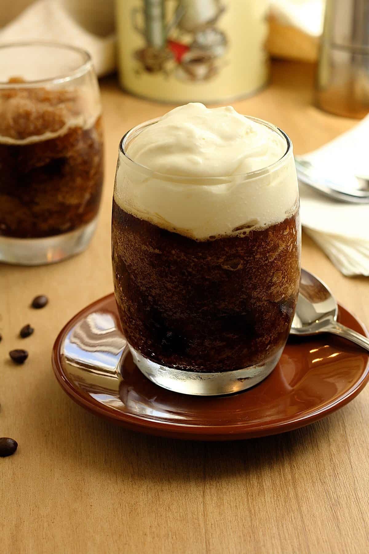 Glasses filled with coffee granita topped with whipped cream on dish with spoon.
