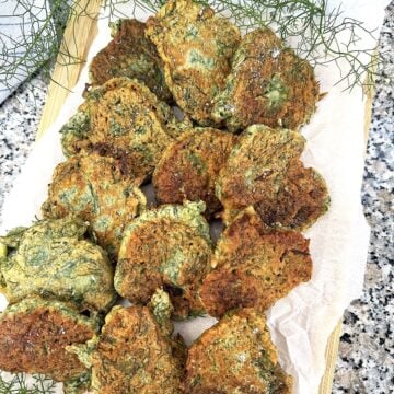 Sicilian wild fritters (frittelle di finocchietto) layered on wood board with fennel fronds around them.