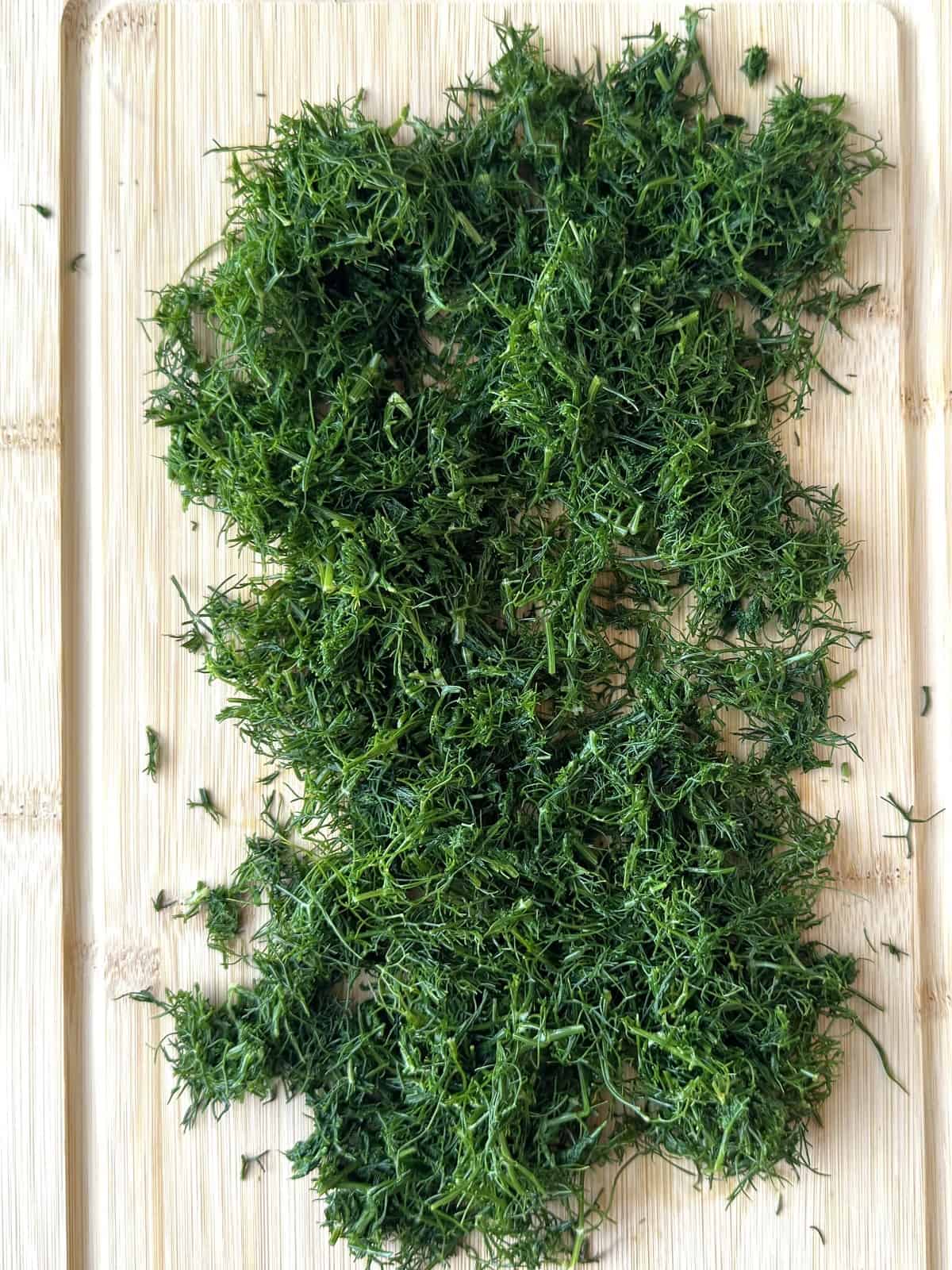 Finely chopped boiled wild fennel on wood board for fritters recipe.