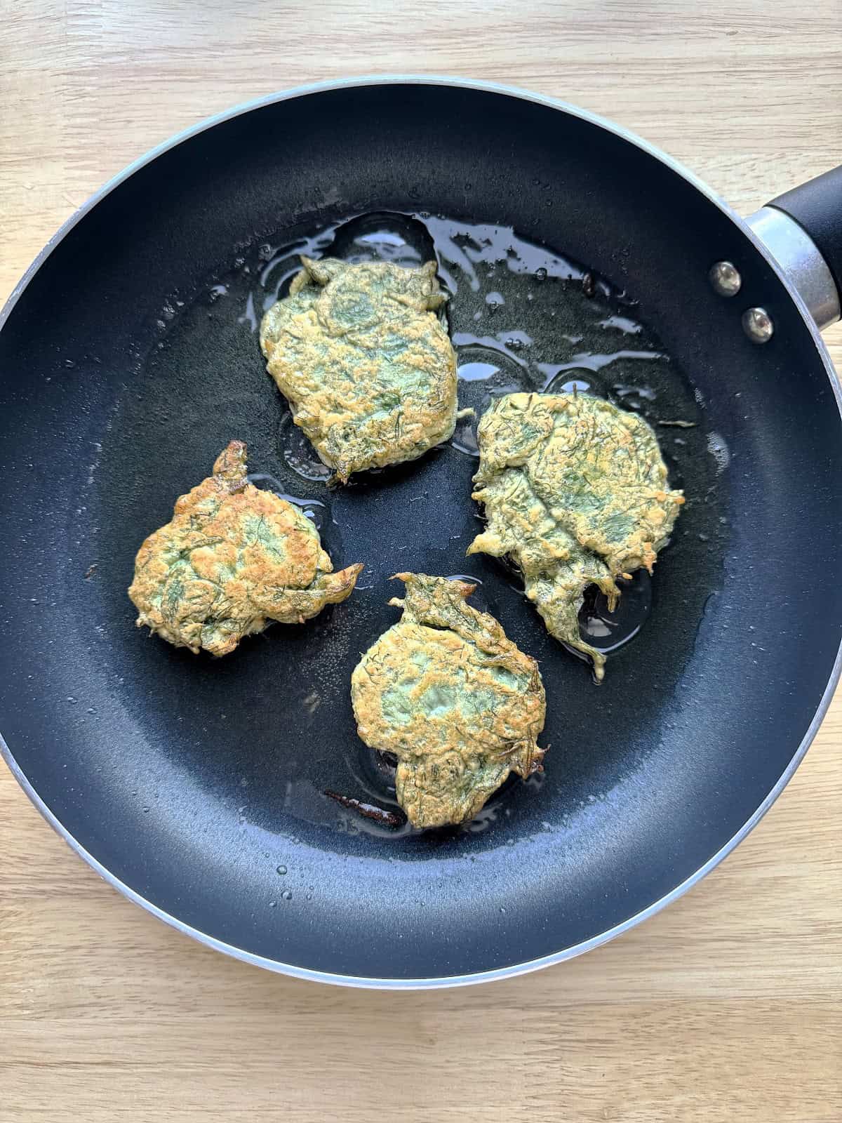 Wild fennel fritters frying in olive oil in skillet.