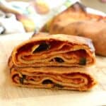 Sicilian layered scaccia with tomato sauce and caciocavallo cheese cut open to reveal layers on wood board.