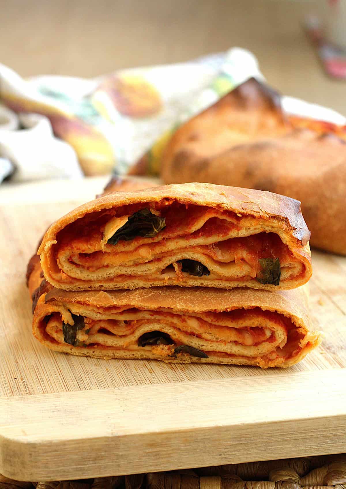 Sicilian layered scaccia with tomato sauce and caciocavallo cheese cut open to reveal layers on wood board.