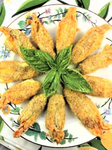 Breaded stuffed zucchini blowers with ricotta on plate with basil leaves.