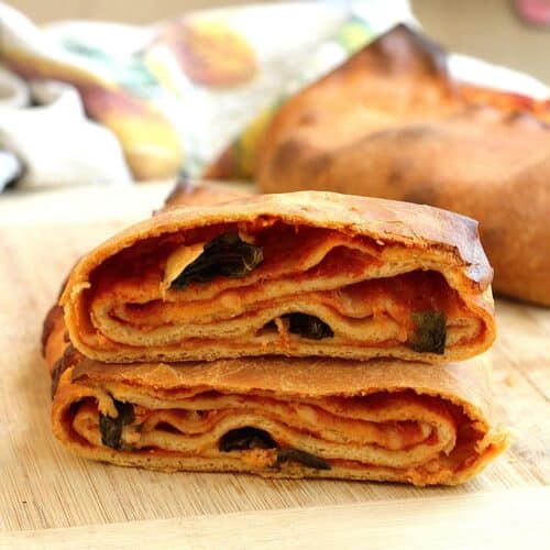 Sicilian scaccia Ragusana bread cut open to revela layers of dough, sauce and cheese.