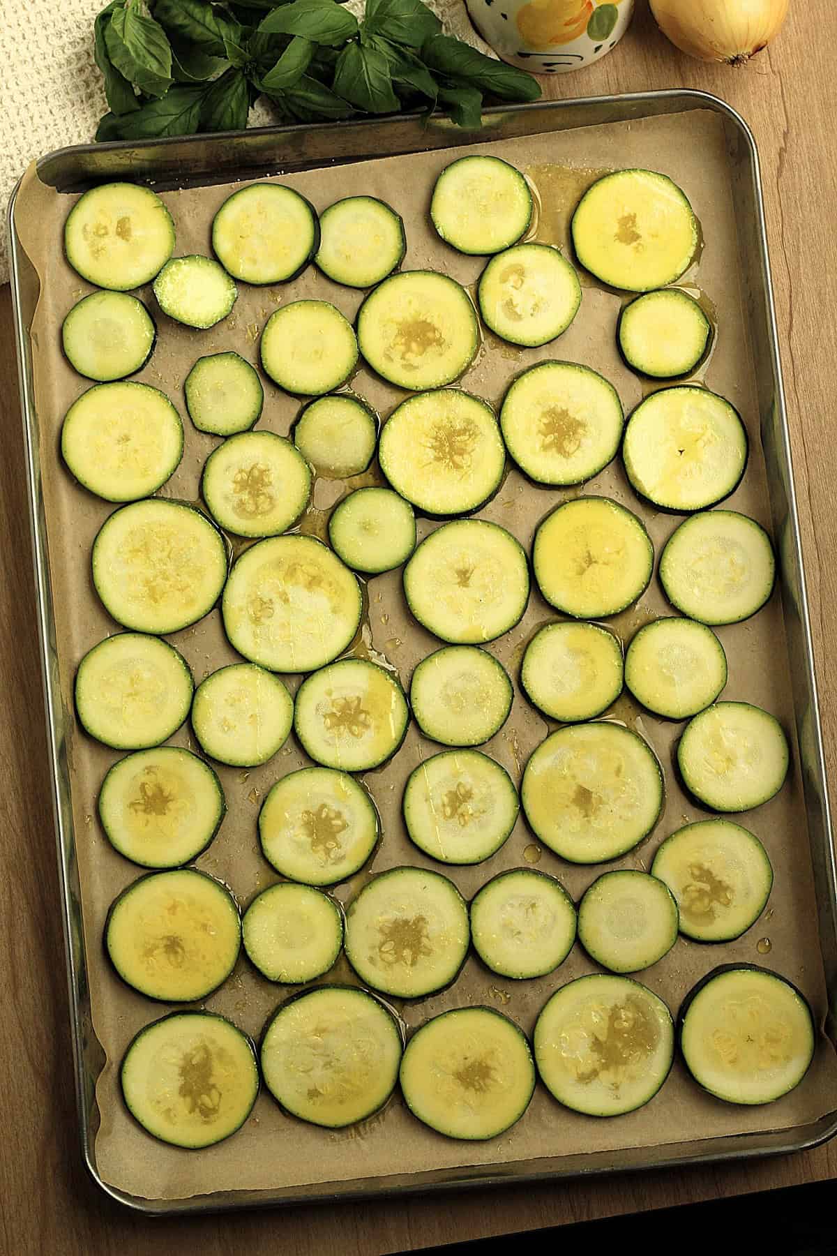 Thinly sliced zucchini on baking sheet coated with olive oil.