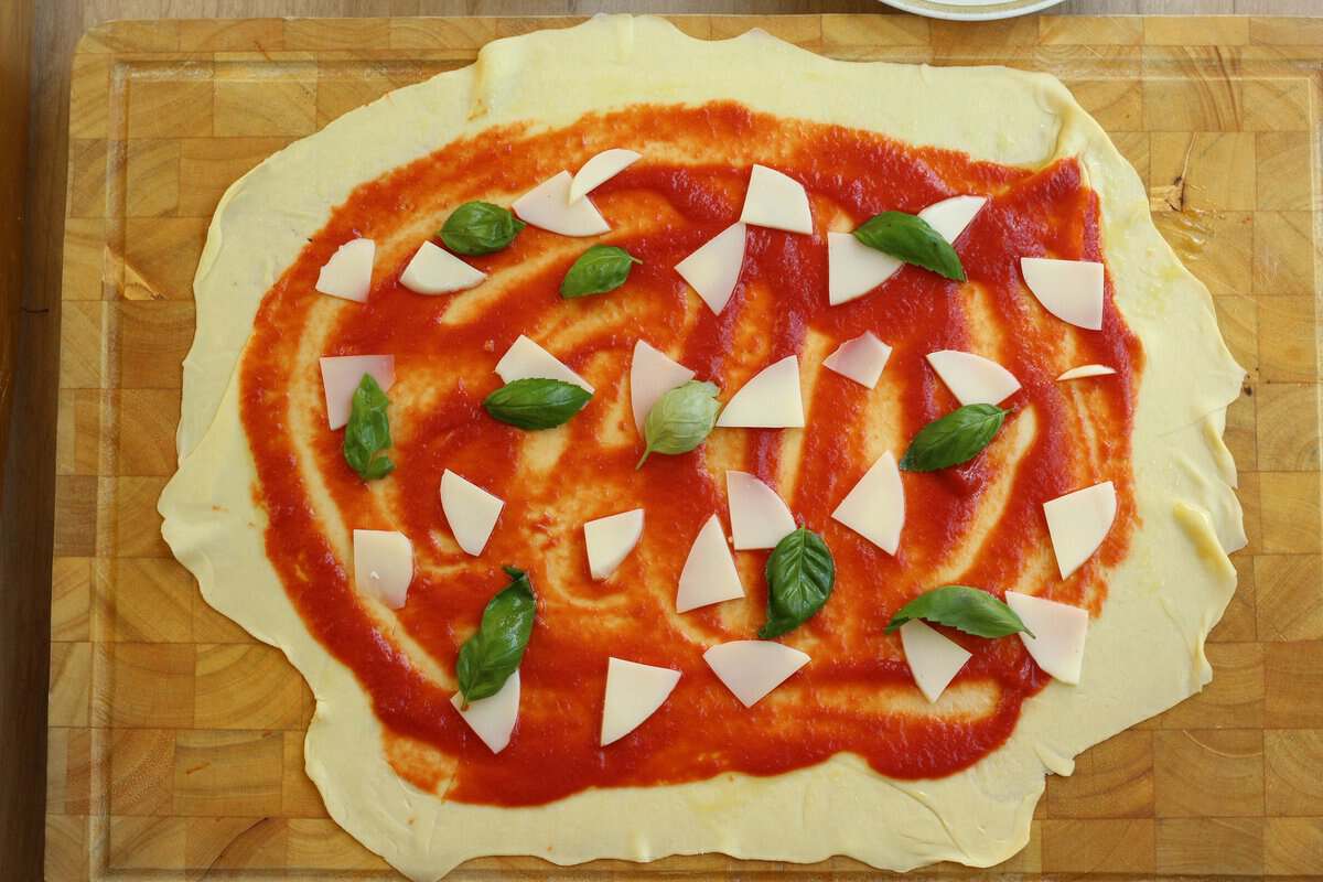 Sheet of semolina dough flattened and covered with tomato sauce, cheese and basil leaves.